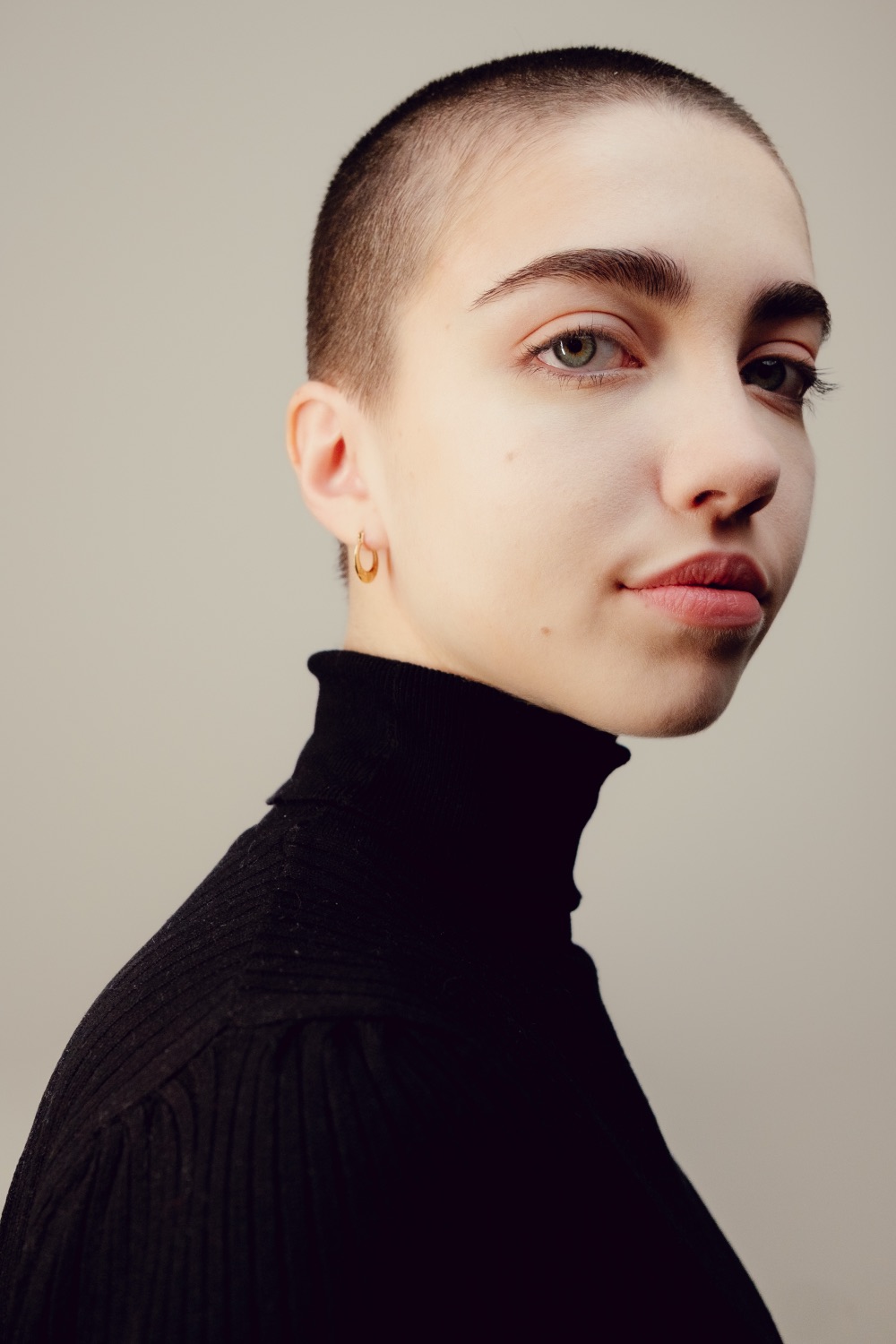 Studio portrait in profile with a gold earring, soft neutral backdrop